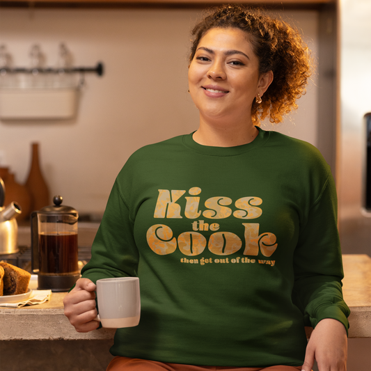 Smiilng boss woman wearing a sweatshirt that say Kiss the Cook, then get out of the way