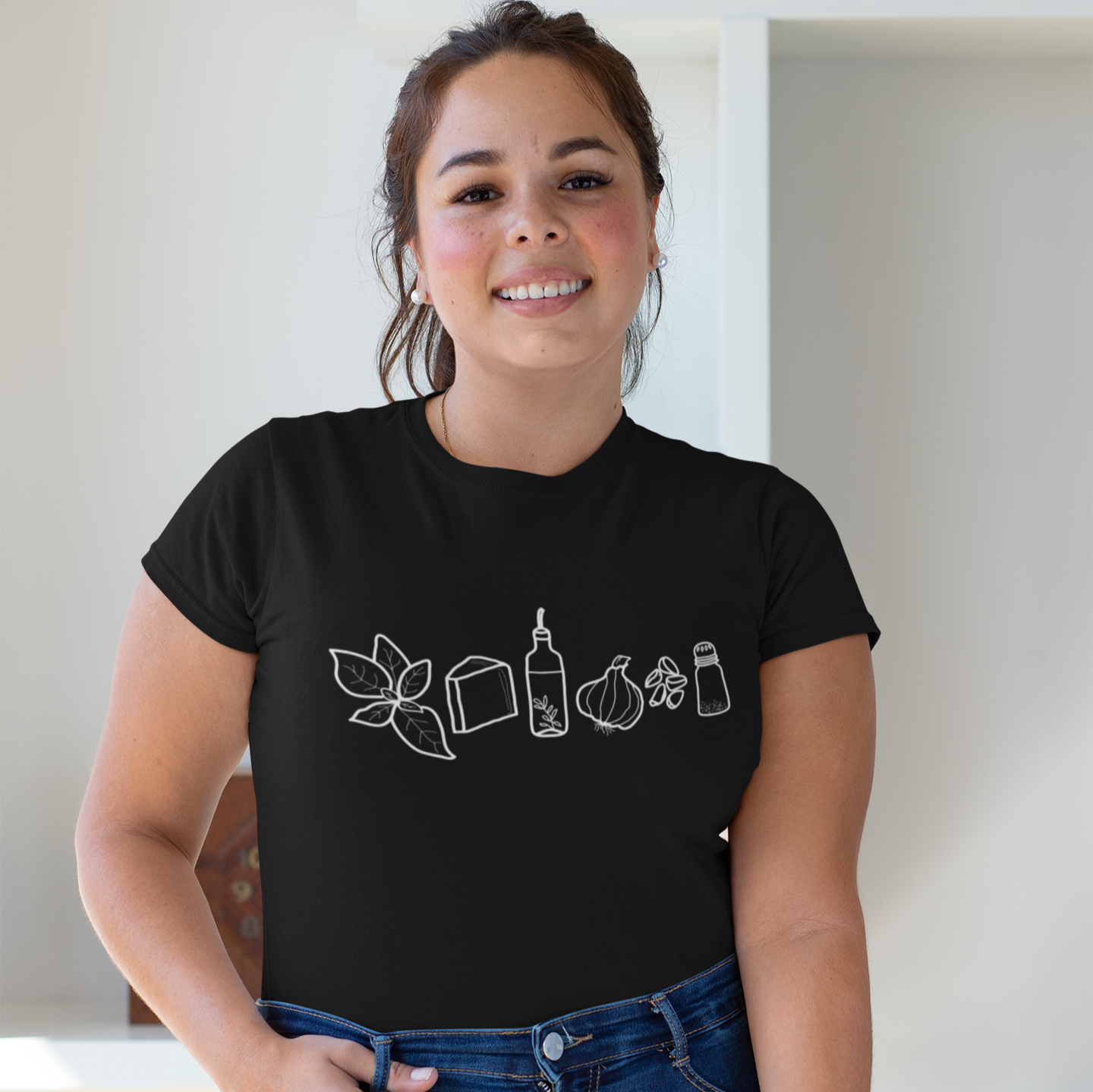 photo of a smiling woman wearing a shirt with hand drawn illustrations of all the ingredients for pesto sauce